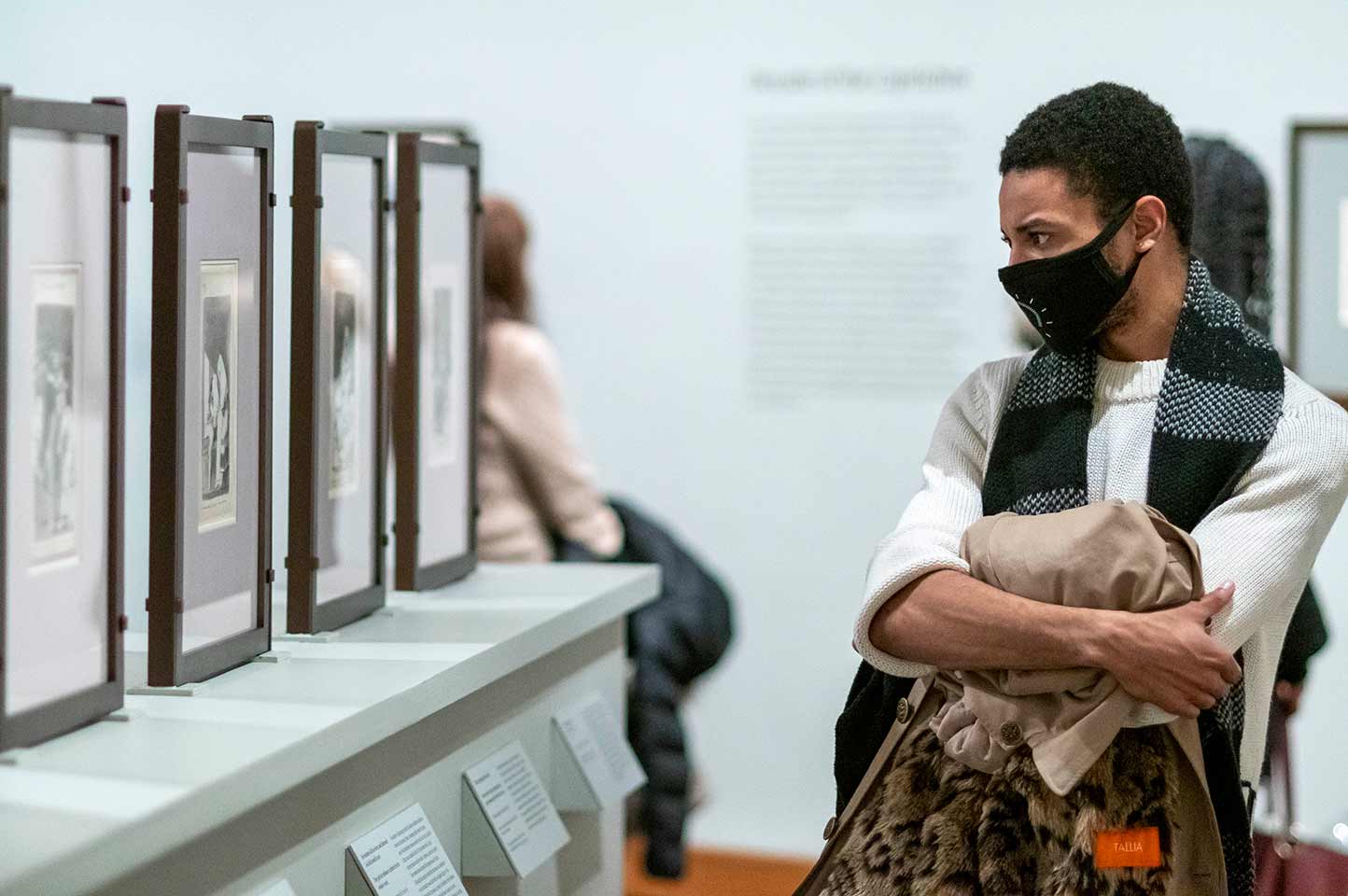 A man crossing his arms, wearing a face mask looking at prints by Goya on display